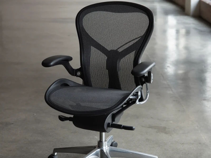 Sedia ergonomica con schienale a rete e braccioli regolabili su cemento levigato